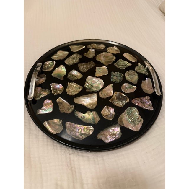 A stunning vintage round black lacquer tray inlaid with dozens of natural abalone shell pieces, each one catching light...