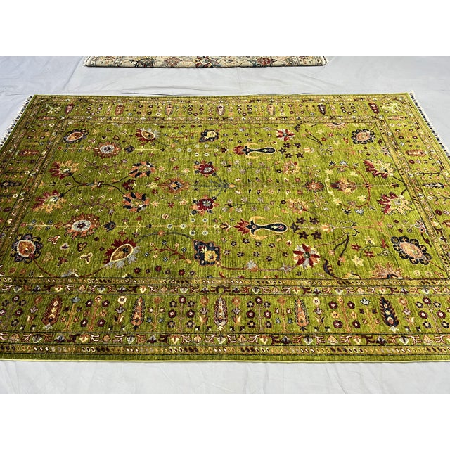 This green Afghan Sultani wool rug features a Persian-inspired floral design with scrolling vines, flowering branches,...