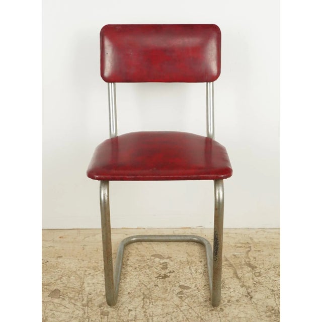Mid Century style dining chairs featuring a red vinyl seat and back rest, and a steel tube frame. Good condition with...