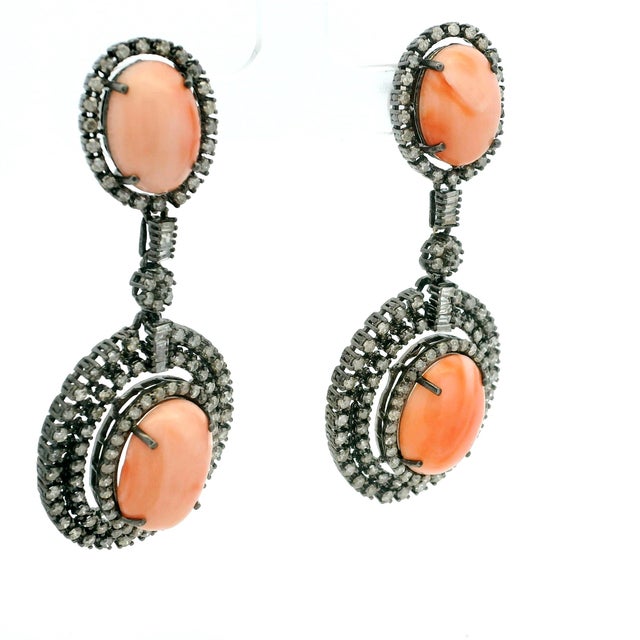 A striking pair of Indian drop earrings crafted in oxidized silver and set with vibrant natural coral cabochons accented...