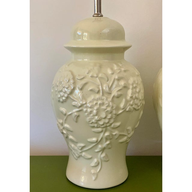 A pair of white, chrysanthemum embossed, chinoiserie set of table lamps. The ginger jar shape gives the lamps a classic...