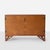 This teak sideboard sits on an angular base and features two internal shelves, three drawers and patinated brass hinge...