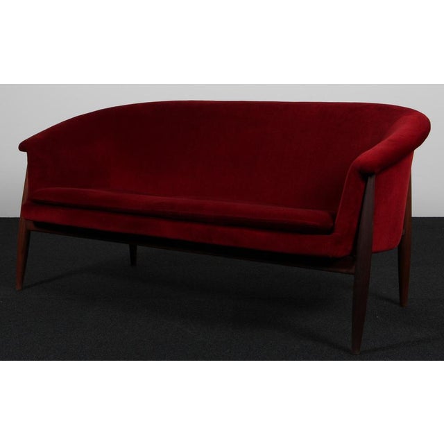 Johannes Andersen two seat sofa with frame of teak. Upholstered with deep red velvet. Made by Trensum. This piece is...