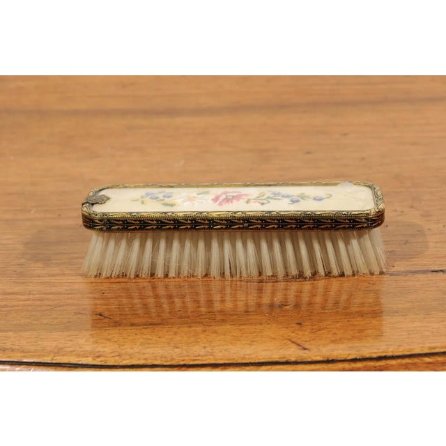 An English clothes brush from the 19th century, with petit point décor on silk and brass borders. Born in England during...