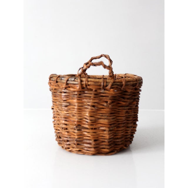 Vintage handwoven wicker basket featuring a rounded form, sturdy woven construction, and twisted loop handles at either...