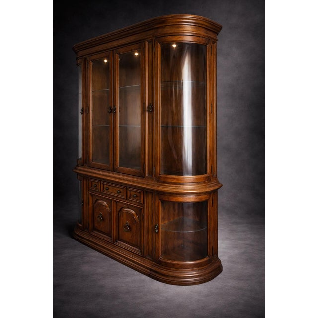 A monumental mid-century Colonial Revival oak china cabinet featuring curved glass display ends, original glass shelving,...