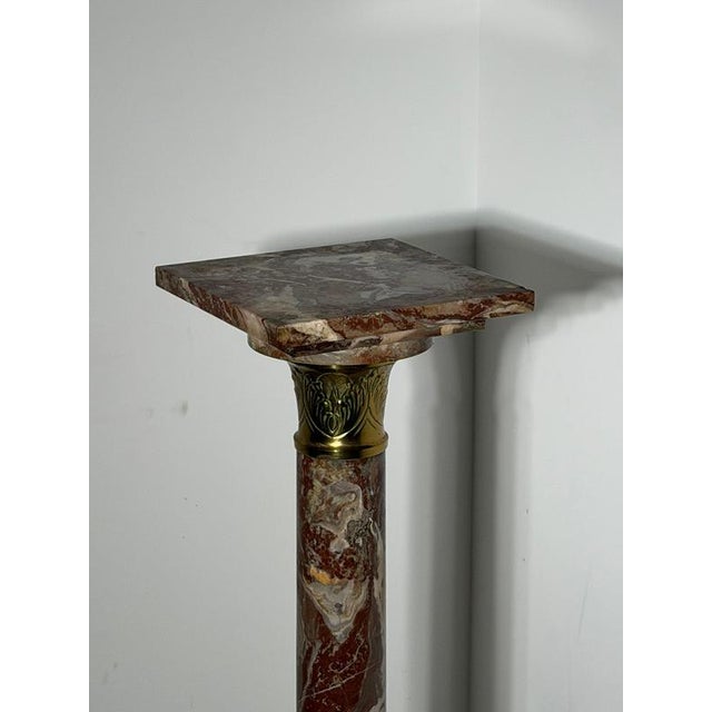 A striking antique marble pedestal featuring richly veined red and pink marble with elegant gilt bronze capitals and base...