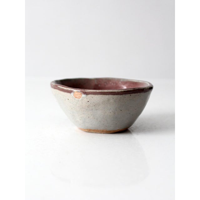Vintage handmade studio pottery bowl featuring a softly rounded form, speckled gray glaze, and a rich mauve interior. The...
