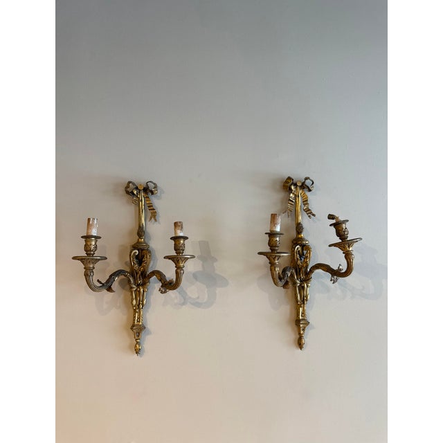 Pair of French Gilded Iron Sconces, circa 1900, each featuring two gracefully curved arms and an elegant bow motif. With...