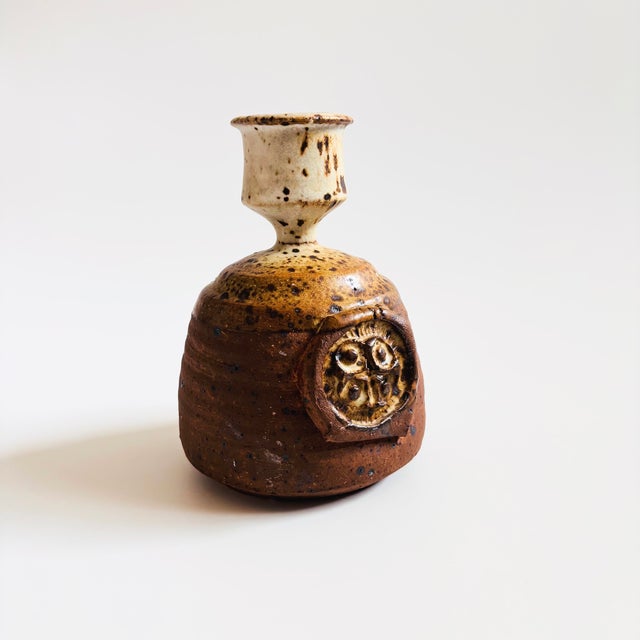 A vintage studio pottery candle holder. Two toned speckled brown and gray glazes with an applied design on the front and...
