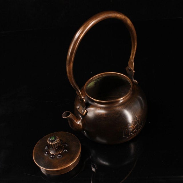 This is a finely crafted antique copper teapot, hand-hammered and featuring ornate gemstone inlays. The body is of squat,...