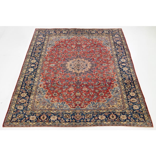 This vintage Persian Isfahan red wool rug features a stunning rosette motif in beige and blue. This rug measures 9'11" x...