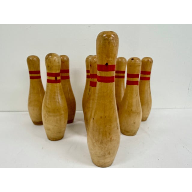 Vintage set of 9 wooden bowling pins with classic red stripe detail and turned wood construction. Natural wood finish with...