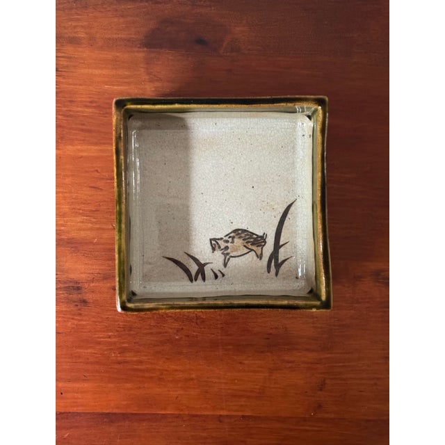 A charming vintage Japanese studio pottery dish featuring a hand-painted wild boar (inoshishi) moving through grasses...