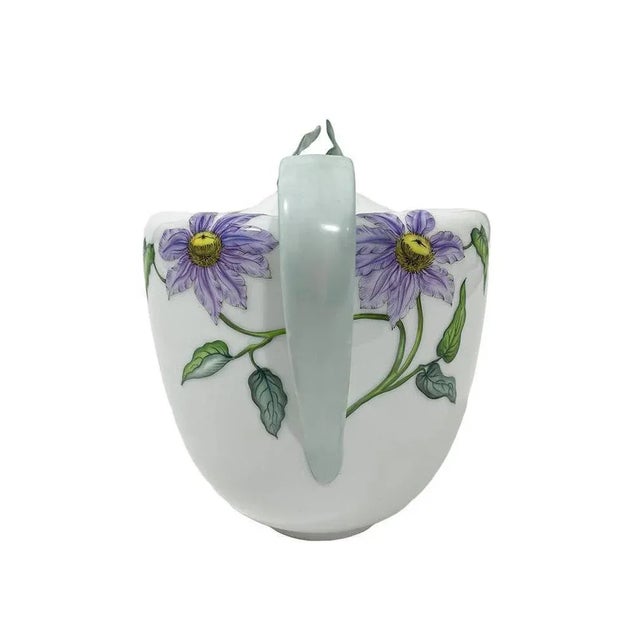 A coffeepot with painted purple clematis flowers in relief on white glossy porcelain. The lid with raised leaves as a...