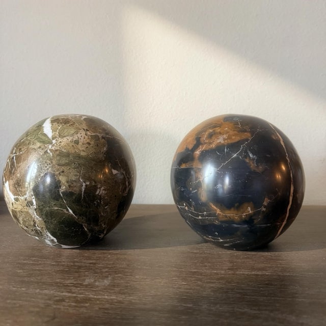 Pair of substantial polished marble decorative spheres, each featuring distinct natural coloration and veining. One sphere...