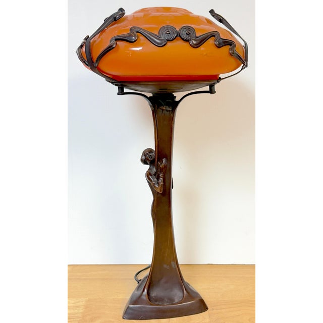 Art Nouveau–Style Figural Bronze Lamp with Acid-Etched Orange Art Glass Shade, Late 20th Century This sculptural figural...