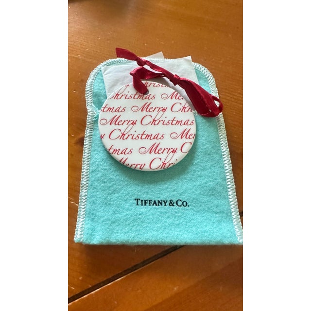 Beautiful Tiffany & Co Round China Ornament with Merry Christmas Ornament with red satin ribbon. Back is marked Tiffany...