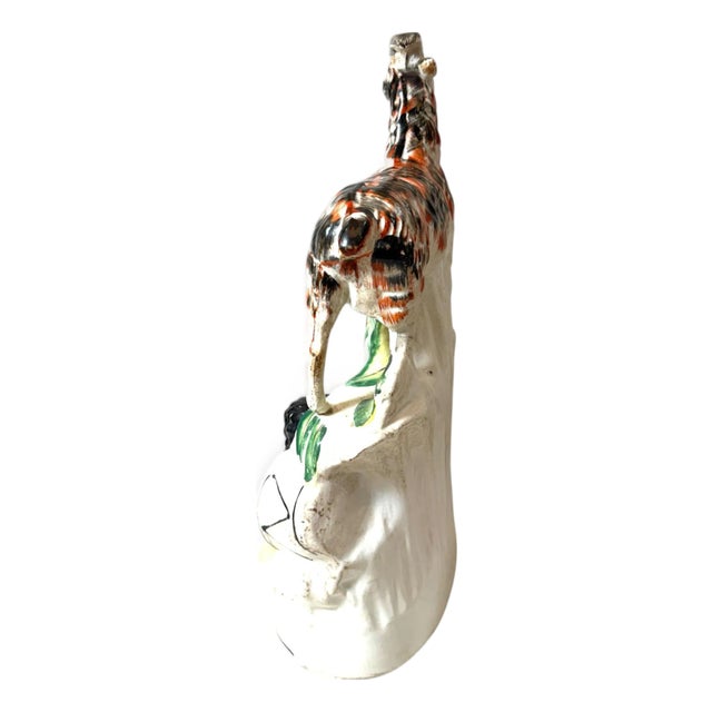 A charming Staffordshire ceramic figure depicting a beautifully spotted goat standing atop a rocky outcrop above a...
