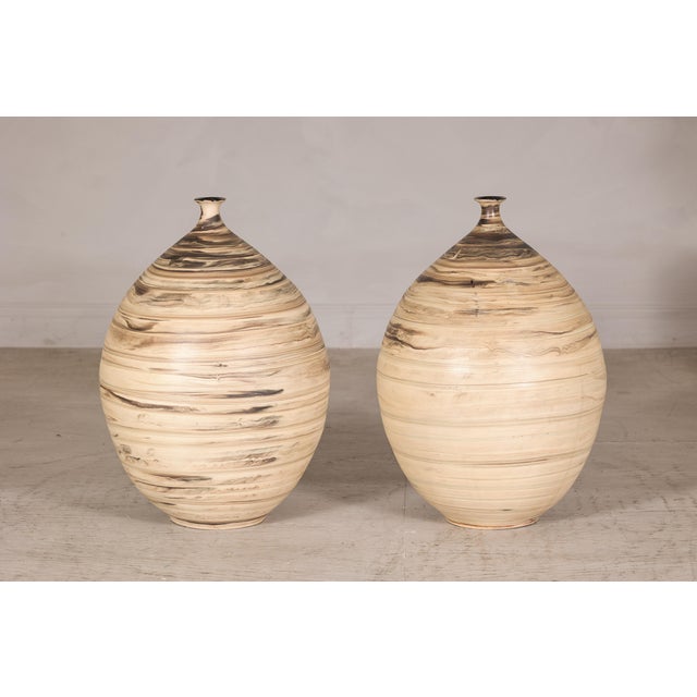 These two large-scale artisan ceramic vases feature a sculptural ovoid form with a narrow, gently flared neck and a softly...