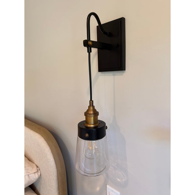 Striking pair of hanging wall sconces combining blackened metal, warm antique brass accents, and clear glass shades. Each...