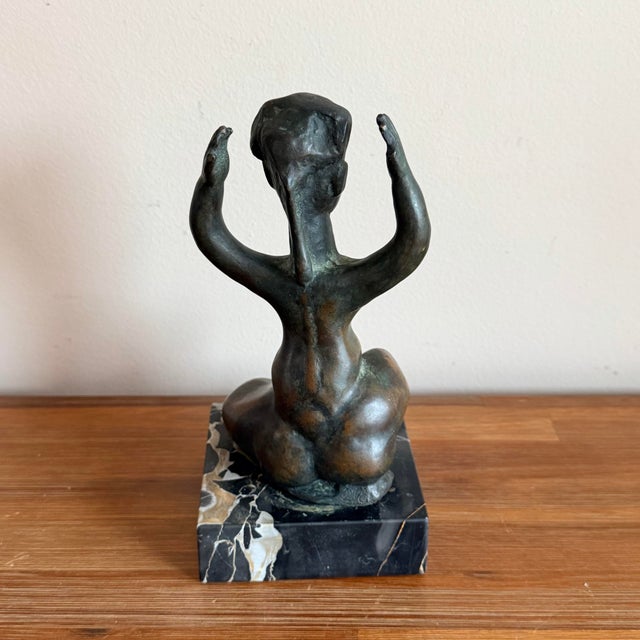 A signed bronze figural sculpture by Benjamin Kopman, mounted on a black marble base. The piece depicts a seated female...