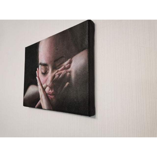 This oil on canvas piece features a close-up of a contemplative figure, their face partially obscured by hands, creating...
