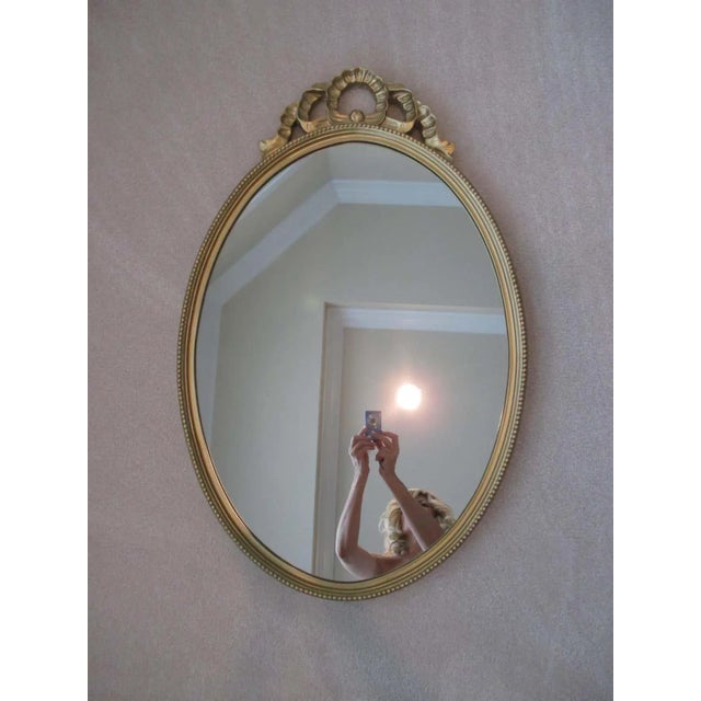 Elegant oval shaped gold mirror with ornate detail. Hanging hardware attached.