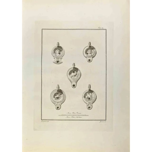 Oil Lamp from "Antiquities of Herculaneum" is an etching on paper realized by Giovanni Guerra in the 18th Century. Signed...