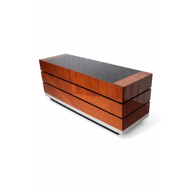 High-gloss lacquered case with wood grain finish. Inset black glass top. Horizontal banded drawer fronts with integrated...