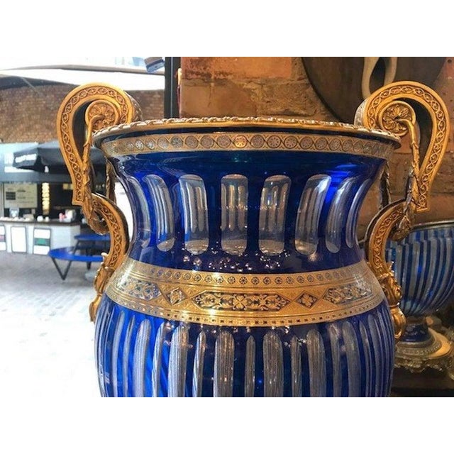 A pair of 20th century blue bohemian crystal urns. The pair feature etched and beveled crystal with gilt bronze handles...