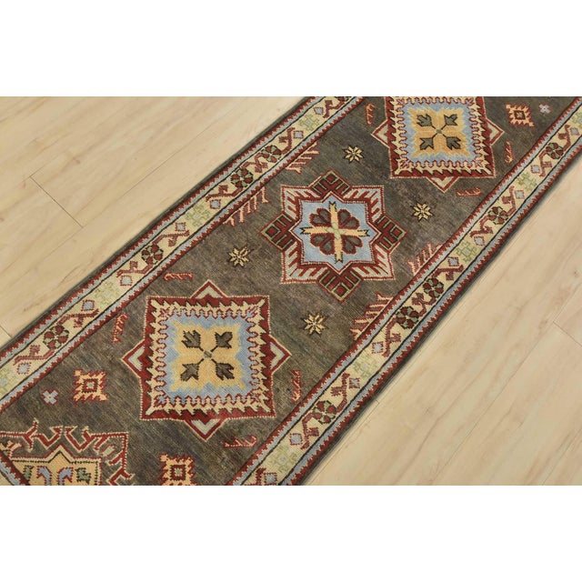 A tribal Caucasian Kazak runner hand-knotted with fine wool on a cotton foundation. This rug features geometric medallions...