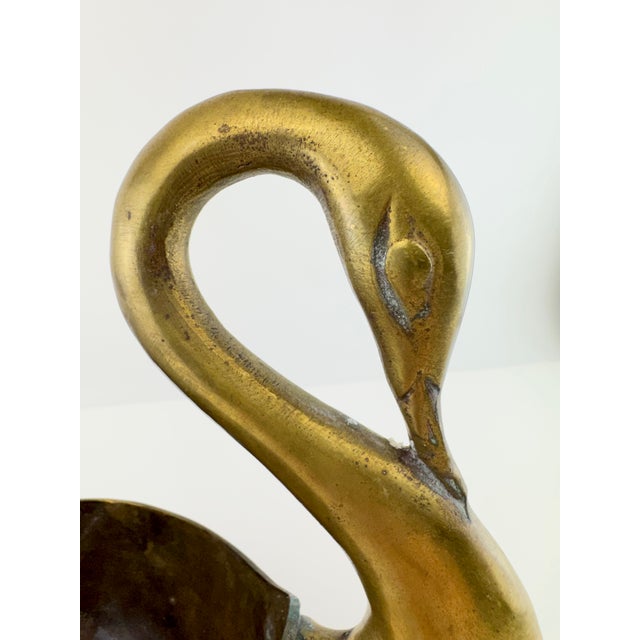 A sculptural vintage brass centerpiece bowl featuring a pair of graceful swans forming dramatic handles at either end. The...