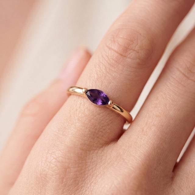 A delicate, minimalist solitaire showcasing a vivid purple marquise-cut amethyst set in an east-west orientation, held...