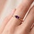 A delicate, minimalist solitaire showcasing a vivid purple marquise-cut amethyst set in an east-west orientation, held...