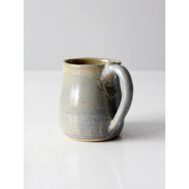 This is a vintage studio pottery mug. Signed by the artist, the handmade mug has a beautiful taupe, blue, and beige mixed...