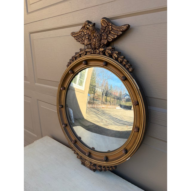 A gorgeous Federal or Regency style convex bullseye wall mirror featuring a carved eagle with open wings standing on olive...