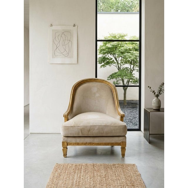 The image shows a classic Louis XVI-style gilded accent armchair (or bergère) featuring a rounded back, neutral cream-...