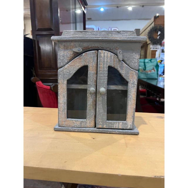 A charming vintage wooden wall cabinet with glass-paneled doors and a beautifully distressed painted finish. The weathered...