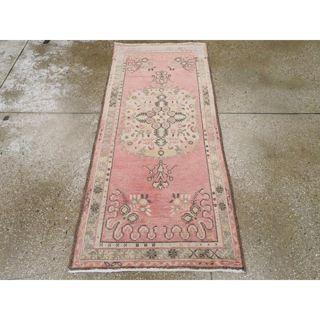 A vintage Turkish Oushak throw rug. The rose-grey semi-open field displays a sand medallion with small stylized flower...