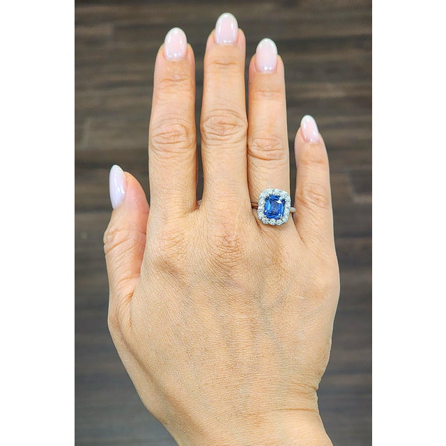 A striking 3.01-carat cushion-cut sapphire commands attention with its deep blue hue. Encircled by a halo of 14 round...