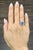 A striking 3.01-carat cushion-cut sapphire commands attention with its deep blue hue. Encircled by a halo of 14 round...