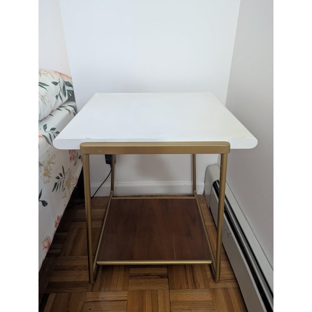 This end table features a white top and a gold wire metal frame. This table is great for placing next to a sofa or bed.