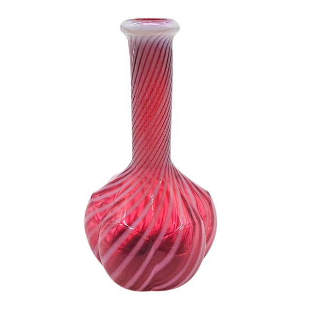 A piece of hand-blown artistry, this cranberry glass bottle carries white spiral ribbons twisting around its bulbous...