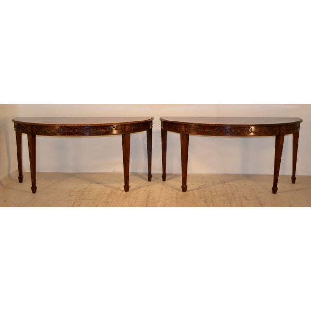 Pair of early 19th century mahogany demilune tables from England in the Adams style. The tables have hand carved decorated...