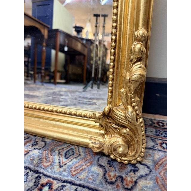 A striking French-style mirror featuring an elaborate scroll top and decorative sides. The frame is fully gilded, giving...