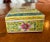 Yellow porcelain box with enamel decoration of flowers and embellishments in green, pink, blue and white. The lid is...