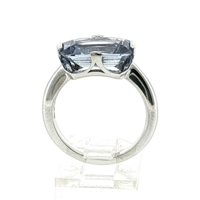 A refined mid-century platinum ring featuring a central emerald-cut, approximately 5-carat pastel blue sapphire. The...