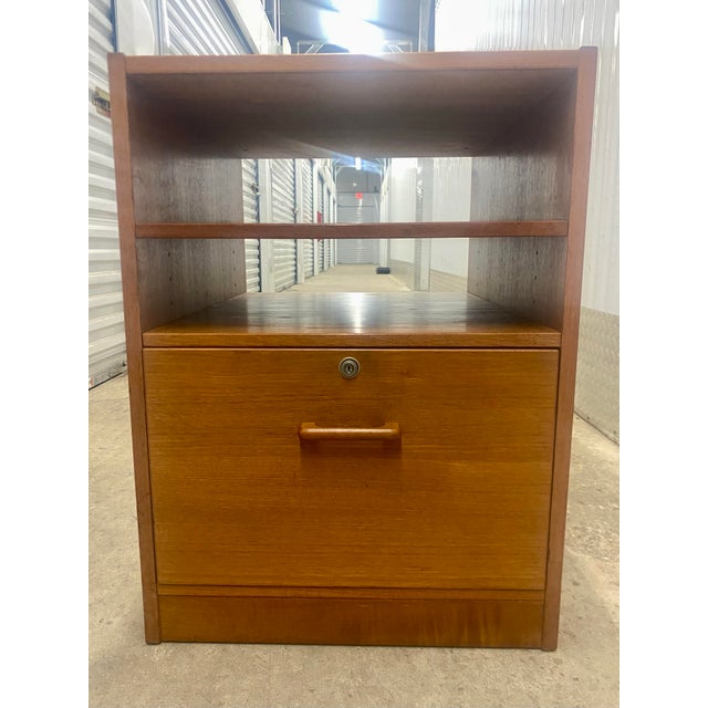 Mid-century modern teak file cabinet with open shelves and a single lockable drawer. It features clean lines and the warm...