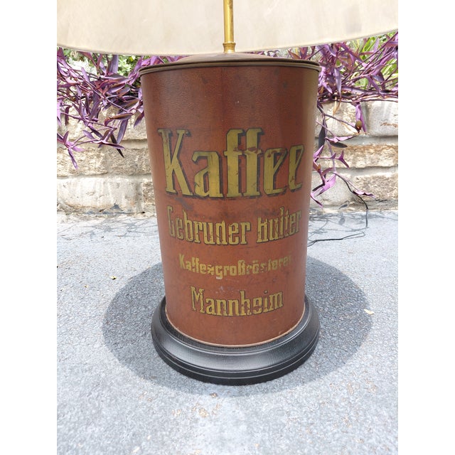A wonderfully distinctive table lamp crafted from an antique German coffee roaster advertising tin, featuring original...